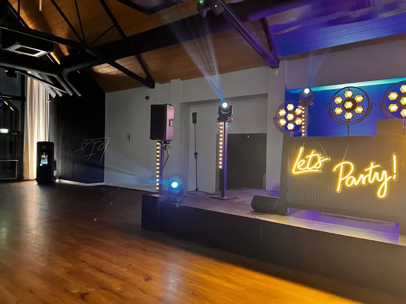 Fotobudka AI ustawiona przy scenie z neonem Let's Party i oświetleniem klubowym - wynajem na imprezy okolicznościowe.