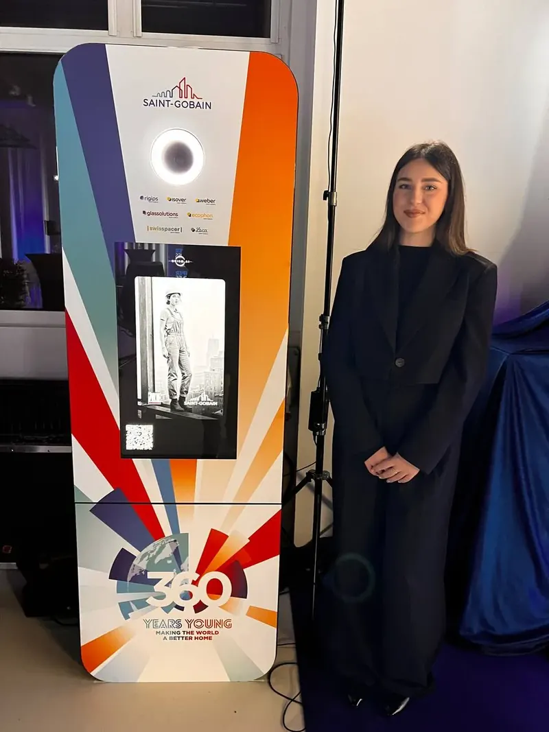 Hostessa przy Fotobudce AI z brandingiem Saint-Gobain 360 Years Young prezentująca portret budowlanki - wynajem brandowany.